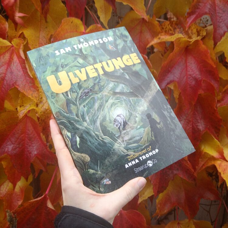 Bogen Ulvetunge holdes op foran et tæppe af røde og orange efterårsblade