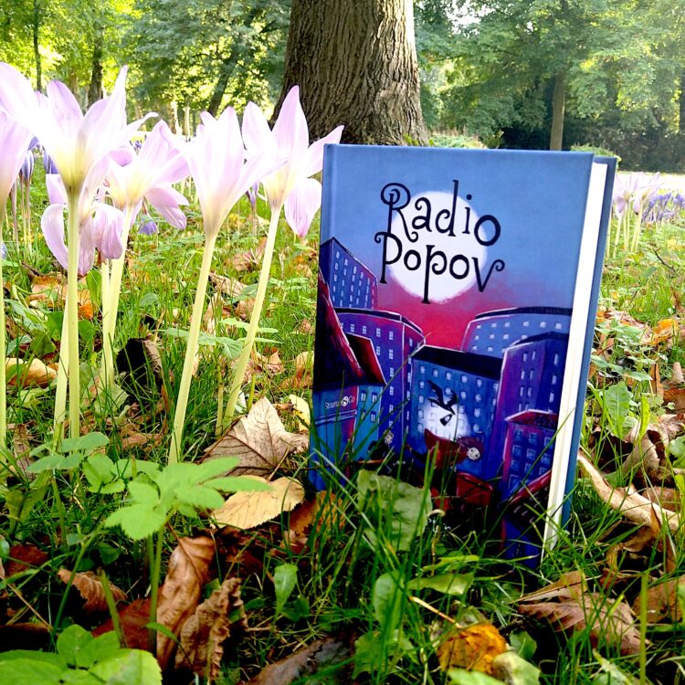 Bogen Radio Popov står på en græsplæne ved siden af lyselilla blomster med træer i baggrunden