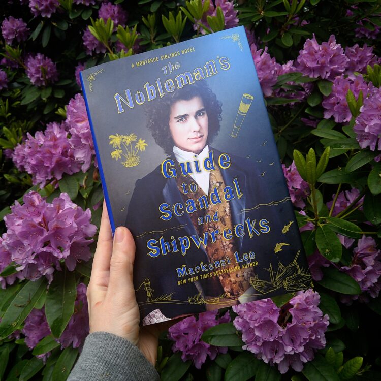 Bogen The Nobleman's Guide to Scandals and Shipwrecks holdes op foran en busk med lilla blomster