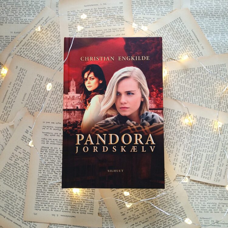 Bogen Pandora Jordskælv ligger ovenpå en masse løser bogsider omgivet af små lys på en lyskæde