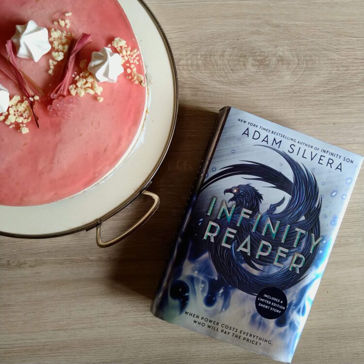 Bogen Infinity Reaper af Adam Silvera ligger ved siden af en lyserød cheesecake med fin pynt på toppen